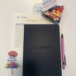 Customized notebook, candy and decal sitting atop a printed meeting agenda